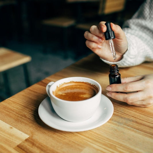 person in a coffee shop putting a few drops of CBD oil into their latte