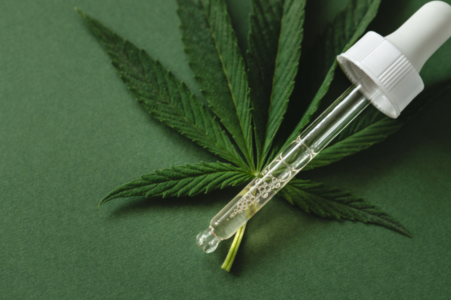 a tincture of oil next to a green cannabis leaf