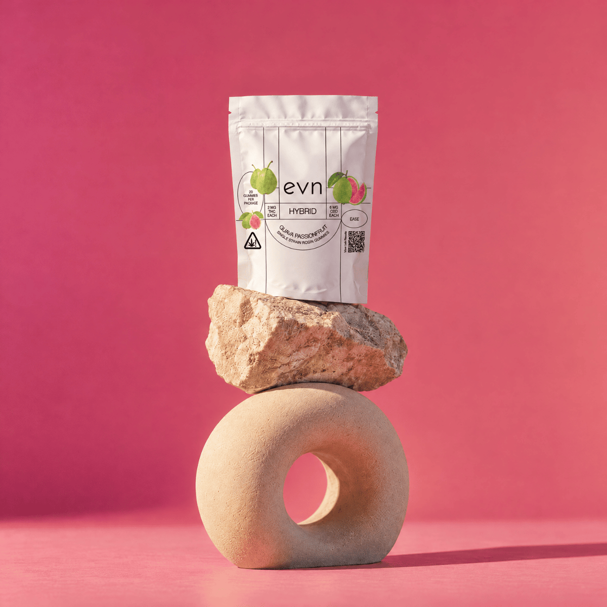 A white stand-up pouch labeled 'evn' with fruit illustrations and 'HIBISCUS' printed on it, styled on top of stacked stones against a pink studio background.