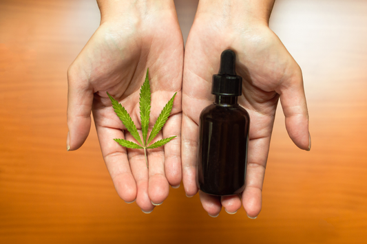hand holding a cannabis leaf in one and a tincture in the other hand