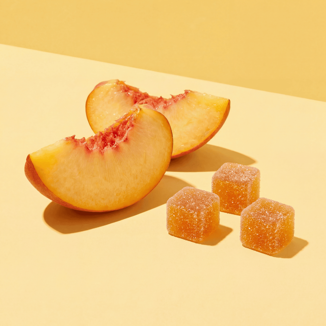 three peach gummies next to slices of peaches